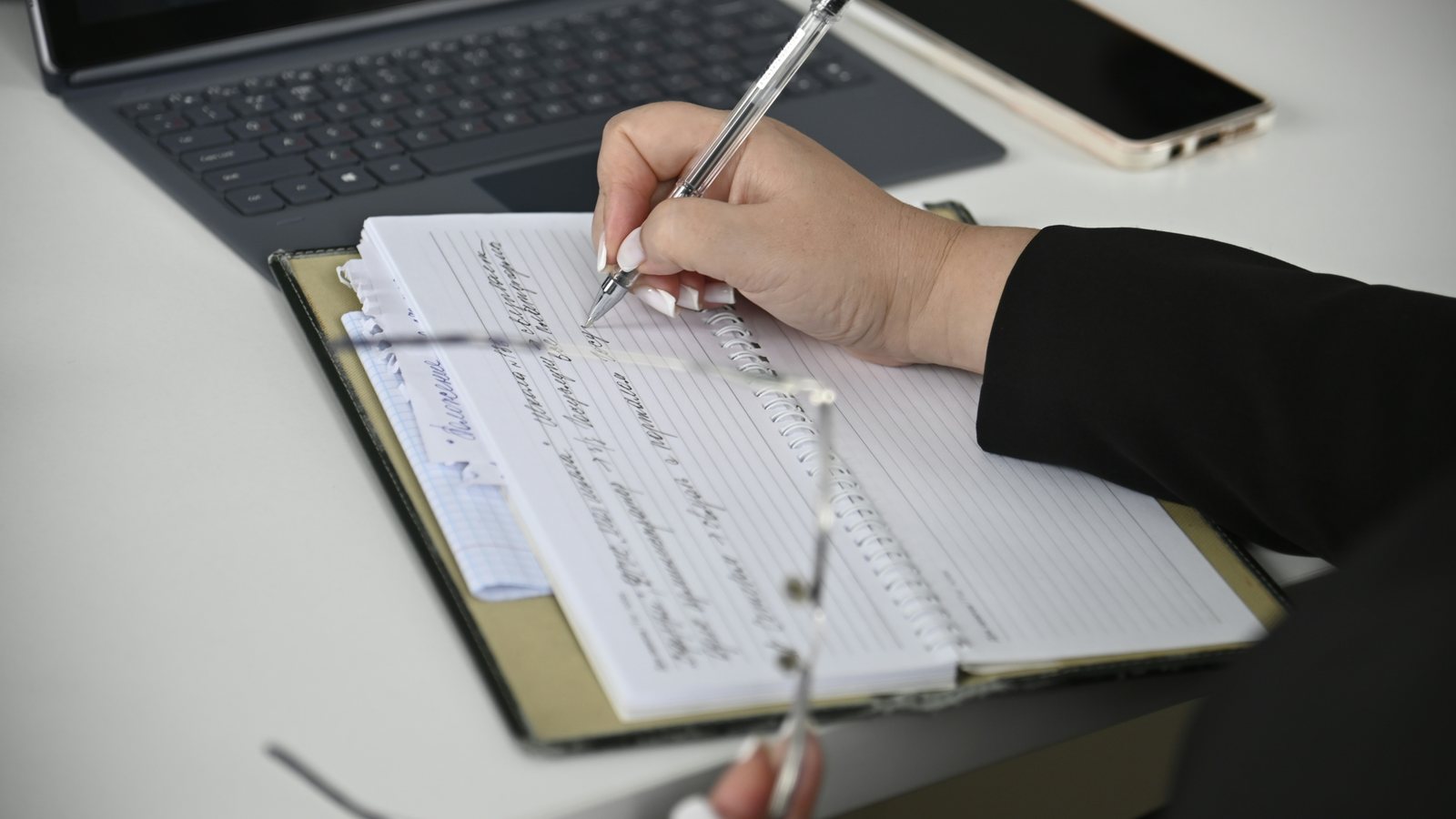 Hand die aantekeningen maakt in een notitieboek naast een laptop
